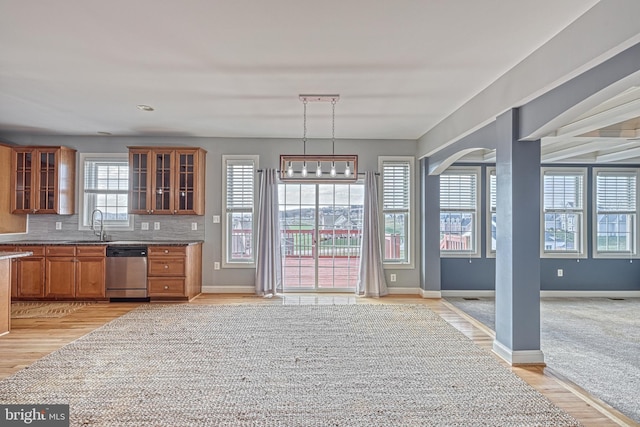 kitchen with sink, tasteful backsplash, light hardwood / wood-style flooring, stainless steel dishwasher, and decorative light fixtures