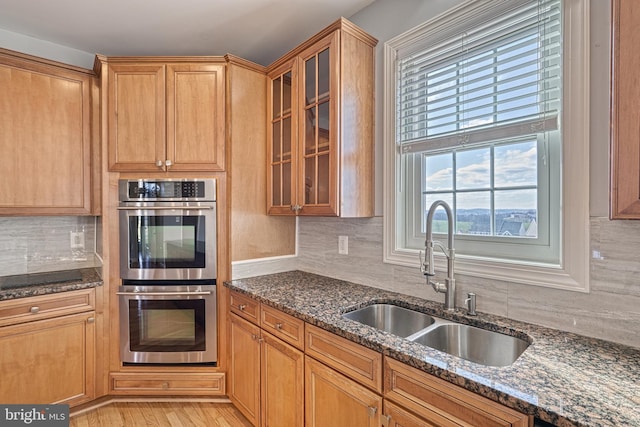 kitchen with stainless steel double oven, sink, and dark stone counters