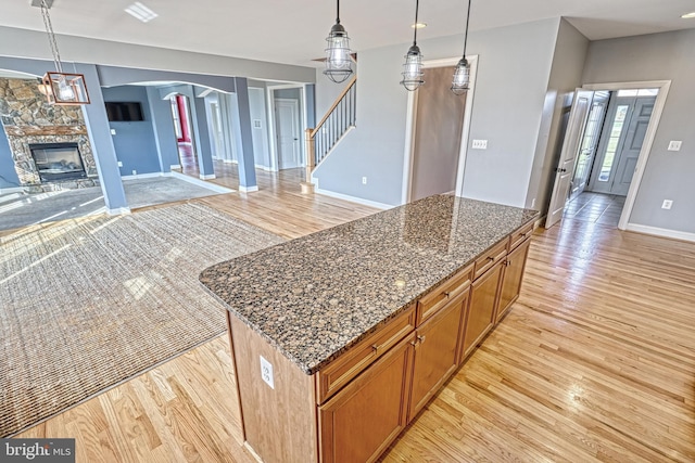 kitchen with pendant lighting, dark stone countertops, a kitchen island, a fireplace, and light hardwood / wood-style floors