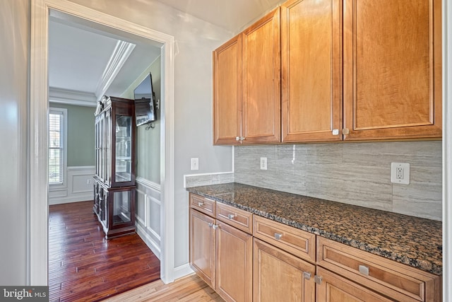 kitchen featuring hardwood / wood-style flooring, backsplash, dark stone countertops, and crown molding