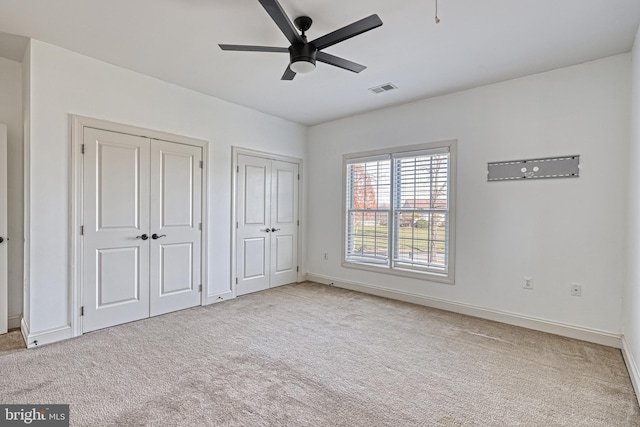 unfurnished bedroom featuring multiple closets, light carpet, and ceiling fan