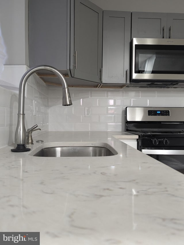 kitchen featuring light stone countertops, sink, stainless steel appliances, gray cabinets, and decorative backsplash