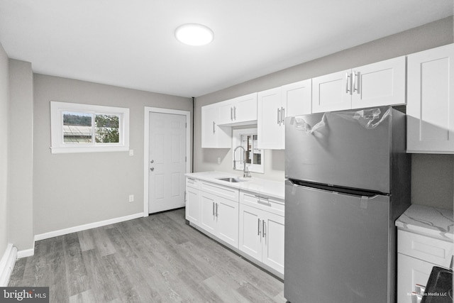 kitchen featuring white cabinets, light wood-type flooring, sink, and stainless steel refrigerator