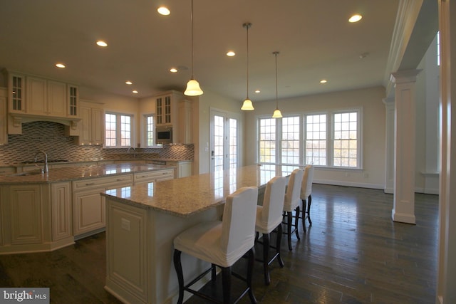 kitchen featuring decorative backsplash, decorative light fixtures, a kitchen island, light stone counters, and a breakfast bar area