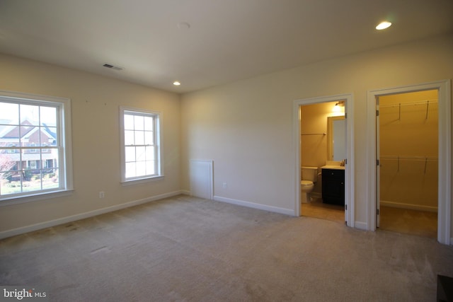 unfurnished bedroom with ensuite bathroom, light colored carpet, a spacious closet, and a closet