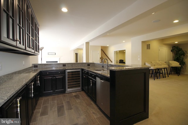 kitchen featuring dishwasher, sink, beverage cooler, kitchen peninsula, and dark stone countertops