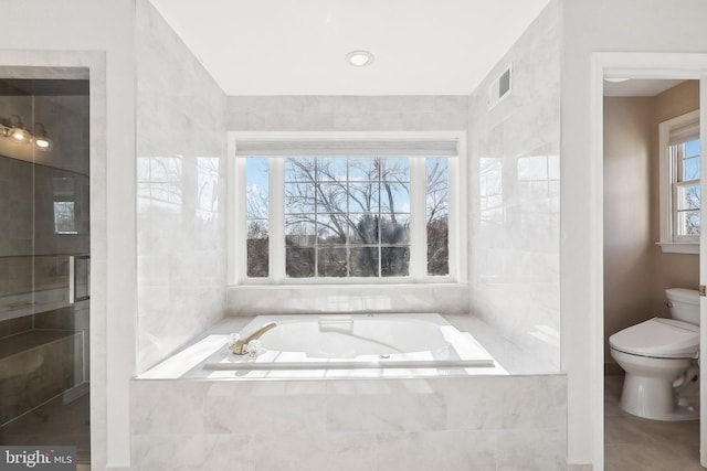 bathroom featuring tile patterned floors, a relaxing tiled tub, tile walls, and toilet