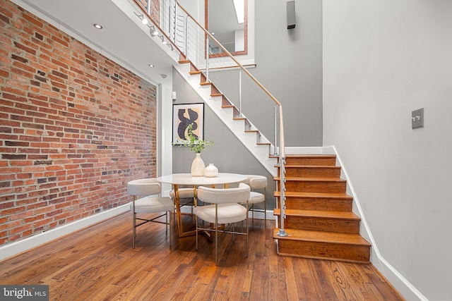 dining room featuring brick wall, wood-type flooring, and a high ceiling