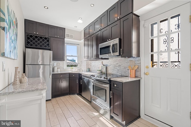 kitchen with light stone countertops, appliances with stainless steel finishes, sink, and backsplash