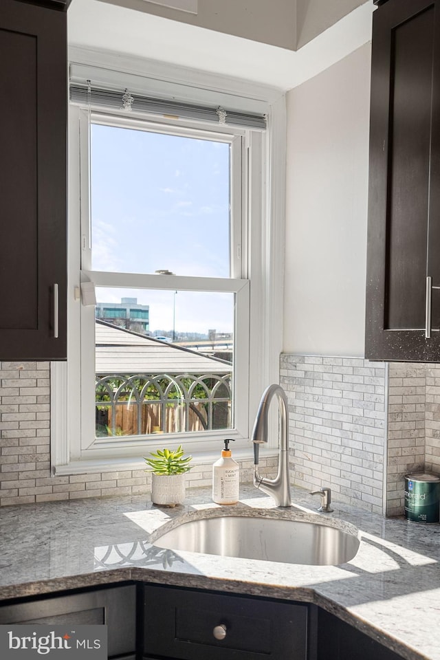 kitchen with tasteful backsplash, light stone countertops, sink, and dark brown cabinets