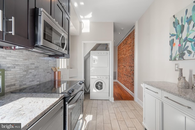 kitchen featuring light stone countertops, appliances with stainless steel finishes, stacked washer and clothes dryer, and light hardwood / wood-style floors