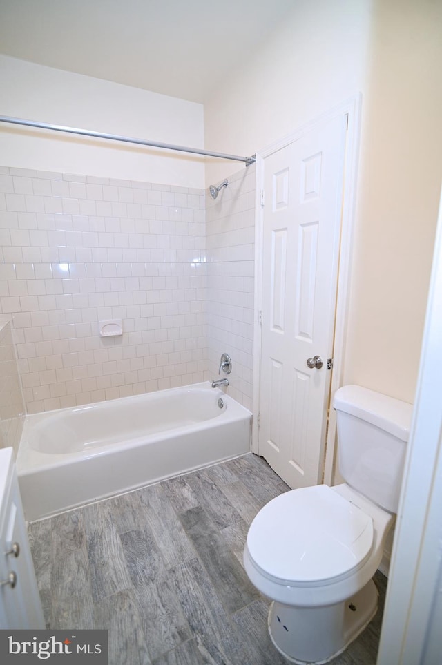 bathroom with hardwood / wood-style floors, tiled shower / bath, and toilet