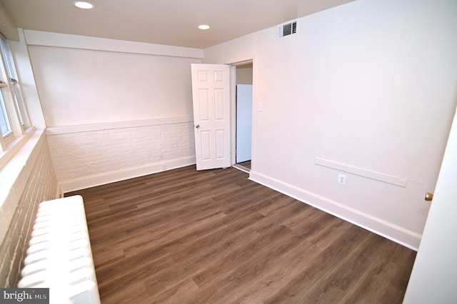 spare room with dark hardwood / wood-style floors and brick wall