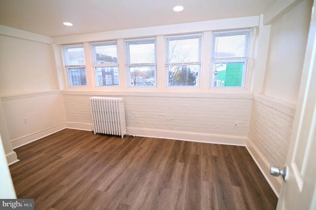 unfurnished room featuring dark hardwood / wood-style flooring, radiator heating unit, brick wall, and plenty of natural light