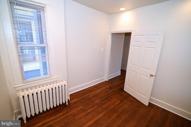 empty room featuring dark hardwood / wood-style flooring, radiator heating unit, and a healthy amount of sunlight