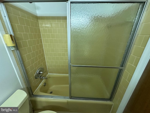 bathroom with toilet and shower / bath combination with glass door