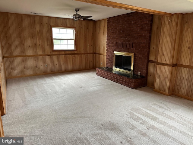 unfurnished living room with ceiling fan, carpet floors, wood walls, and a brick fireplace