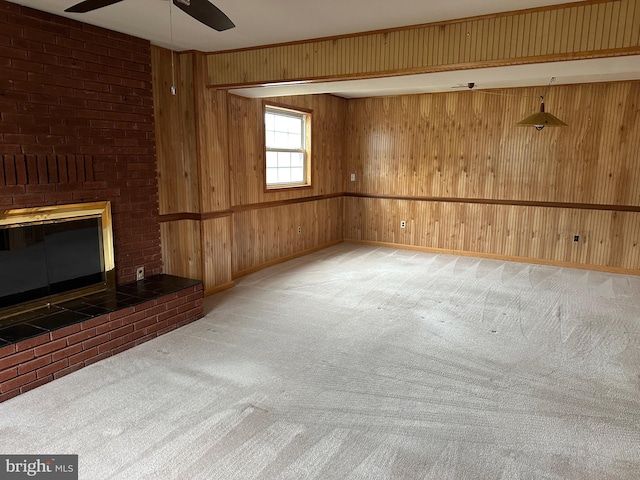 unfurnished living room with carpet flooring, ceiling fan, wood walls, and a fireplace