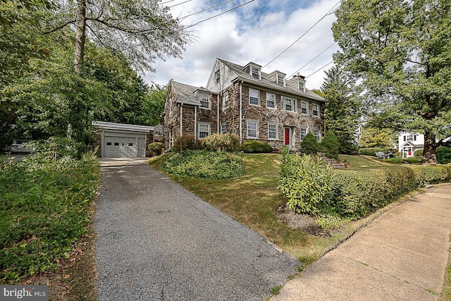 view of front of property featuring an outbuilding, a garage, stone siding, driveway, and a front lawn