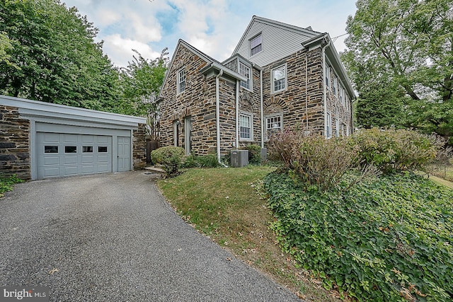 view of front of property with a garage, driveway, stone siding, central air condition unit, and a front lawn