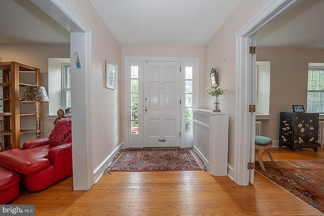 foyer featuring wallpapered walls, light wood-style flooring, and baseboards