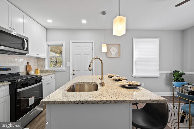 kitchen with stainless steel appliances, light stone counters, and an island with sink