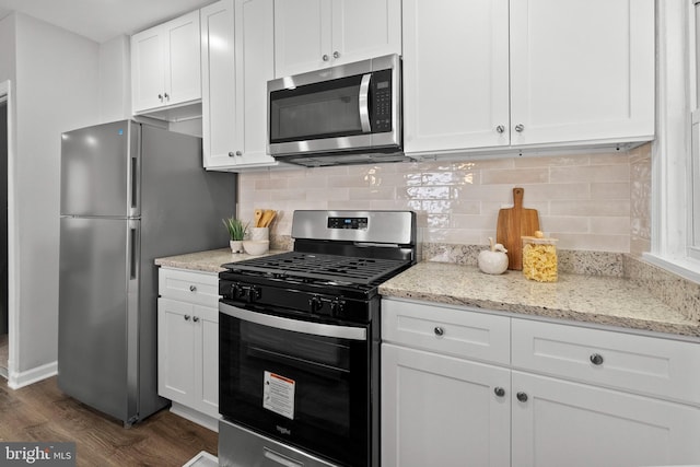 kitchen with backsplash, dark hardwood / wood-style floors, light stone countertops, white cabinetry, and stainless steel appliances