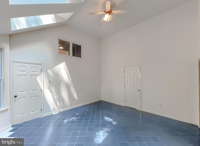 interior space featuring ceiling fan, lofted ceiling with skylight, and dark tile patterned floors