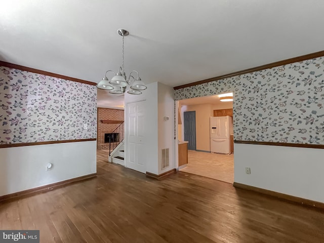 unfurnished dining area featuring a brick fireplace, dark wood-type flooring, ornamental molding, and an inviting chandelier