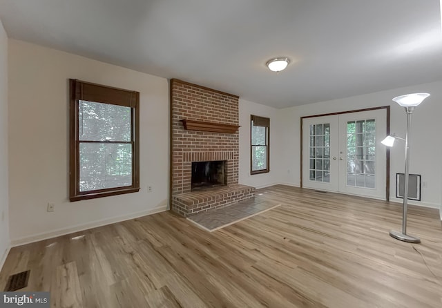 unfurnished living room featuring a brick fireplace, light hardwood / wood-style floors, and french doors