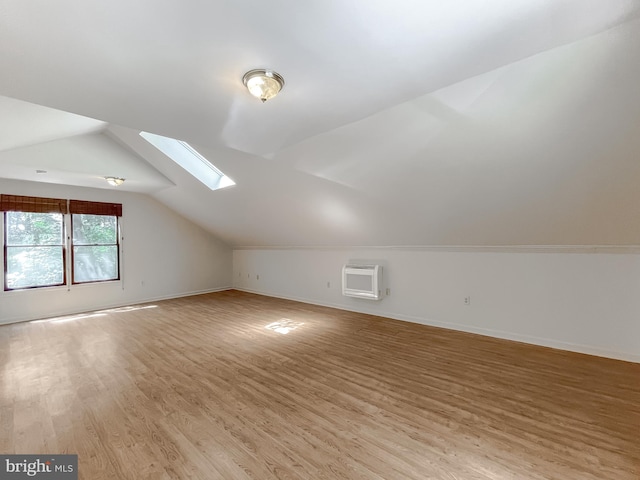 additional living space featuring vaulted ceiling with skylight, a wall mounted AC, and light wood-type flooring