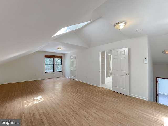 additional living space featuring vaulted ceiling with skylight and light hardwood / wood-style floors