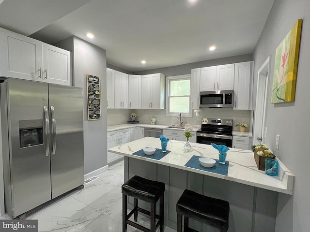 kitchen featuring stainless steel appliances, white cabinetry, and a breakfast bar area