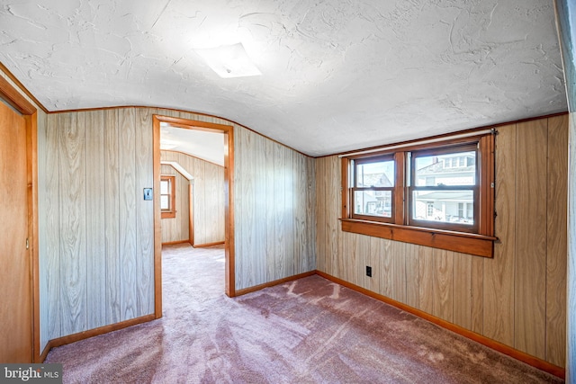 additional living space featuring a textured ceiling, wooden walls, light carpet, and vaulted ceiling