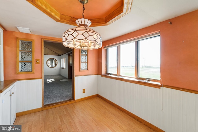 unfurnished dining area featuring light hardwood / wood-style floors, a raised ceiling, and crown molding