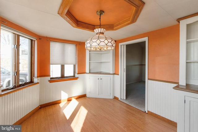 unfurnished dining area with built in shelves, light hardwood / wood-style floors, and a tray ceiling