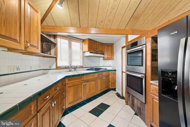 kitchen with under cabinet range hood, tile counters, appliances with stainless steel finishes, and a sink