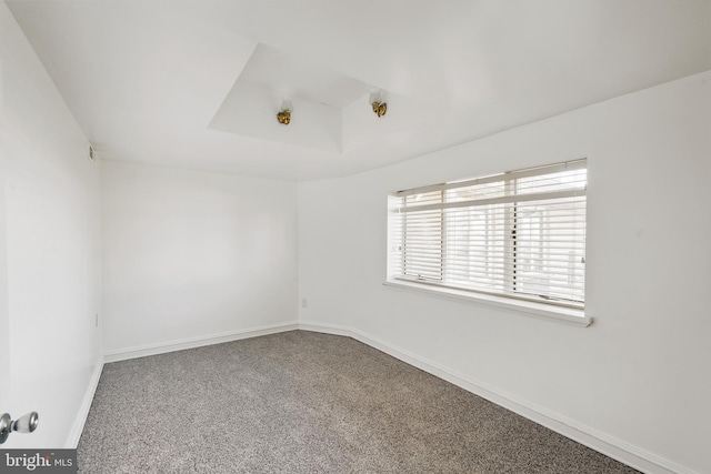 carpeted empty room featuring a raised ceiling and baseboards