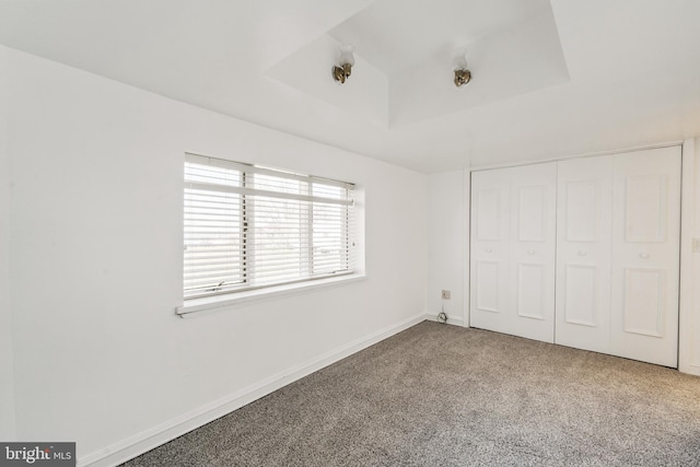 unfurnished bedroom with carpet floors, a raised ceiling, a closet, and baseboards