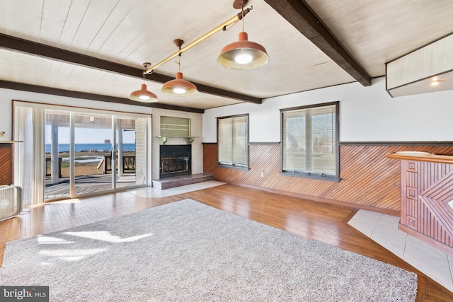 unfurnished living room with beam ceiling, light hardwood / wood-style floors, a wealth of natural light, and wood walls