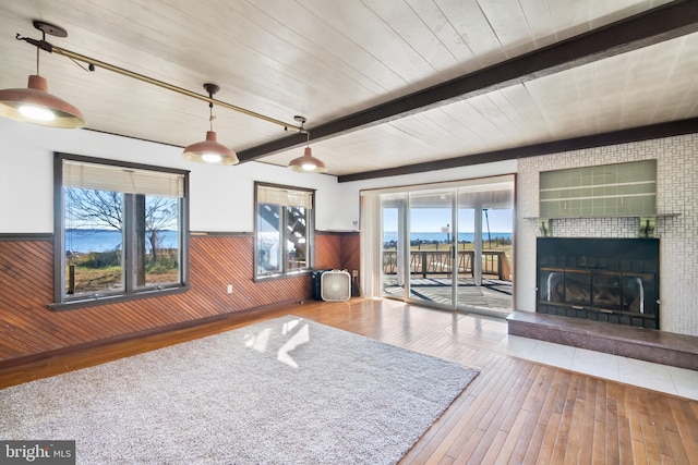 unfurnished living room featuring a fireplace, wood-type flooring, a wealth of natural light, and beamed ceiling