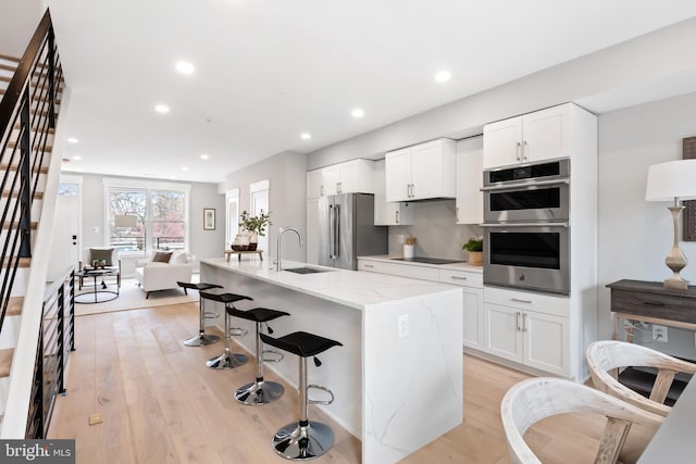 kitchen featuring white cabinetry, sink, stainless steel appliances, an island with sink, and a kitchen bar