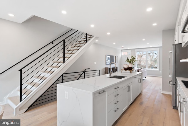 kitchen featuring a center island with sink, sink, light stone countertops, light hardwood / wood-style floors, and white cabinetry