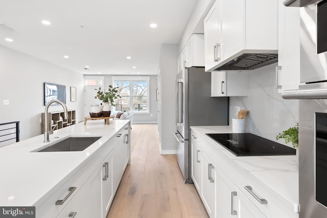 kitchen featuring black electric stovetop, sink, light hardwood / wood-style flooring, light stone counters, and white cabinetry