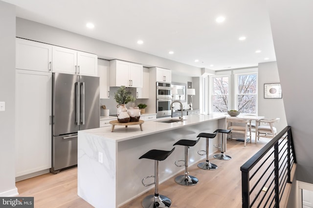 kitchen featuring white cabinets, sink, light stone countertops, light wood-type flooring, and appliances with stainless steel finishes