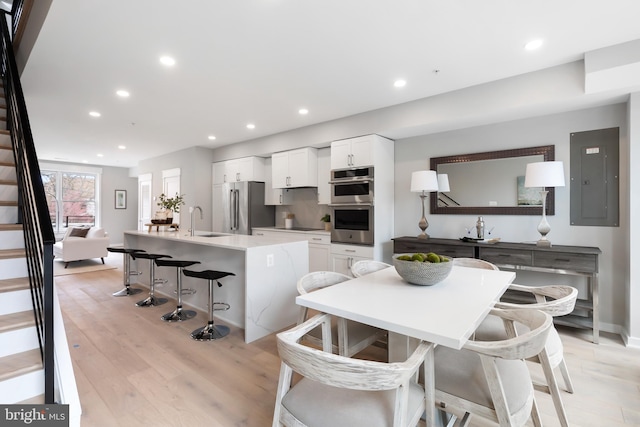 kitchen with a breakfast bar, stainless steel appliances, light hardwood / wood-style flooring, electric panel, and white cabinetry