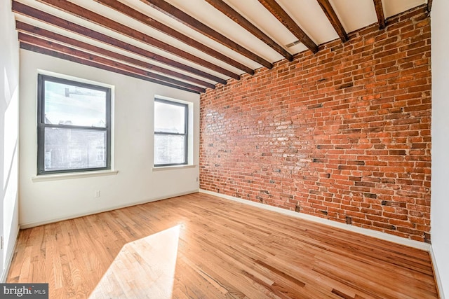 unfurnished room with beam ceiling, light hardwood / wood-style floors, and brick wall