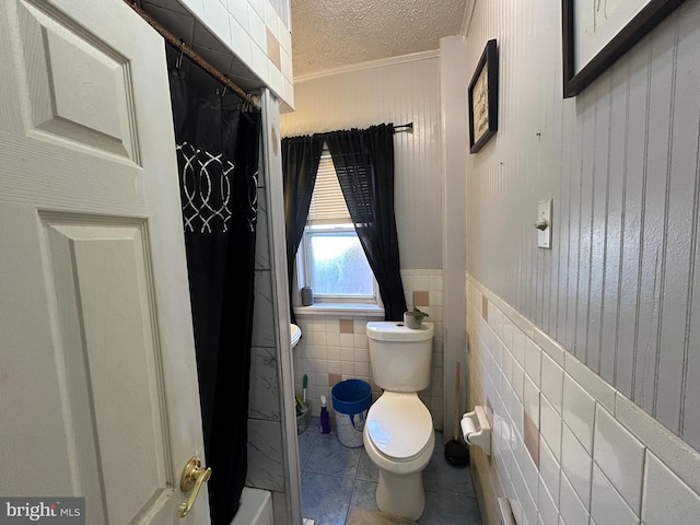 bathroom featuring tile patterned floors, a textured ceiling, toilet, tile walls, and ornamental molding