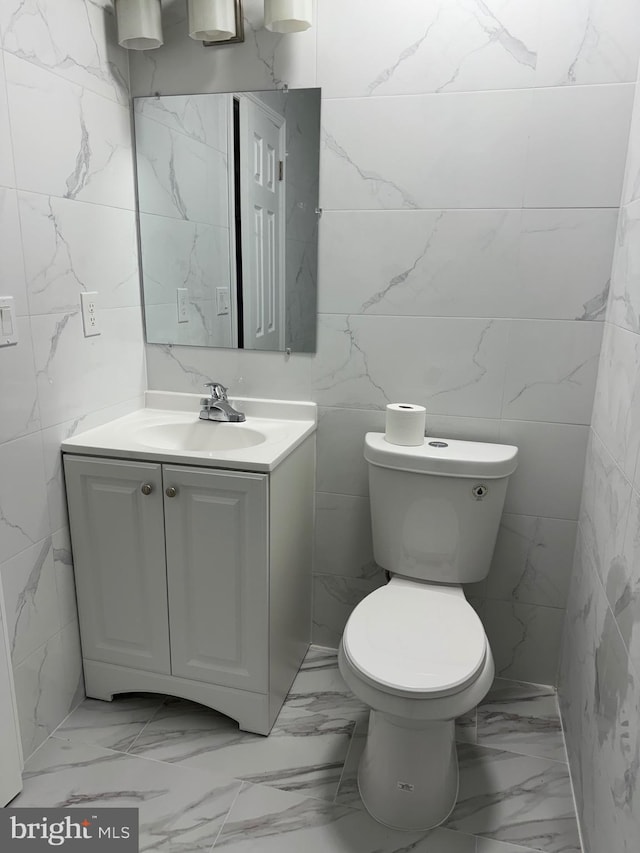 bathroom with vanity, toilet, and tile walls