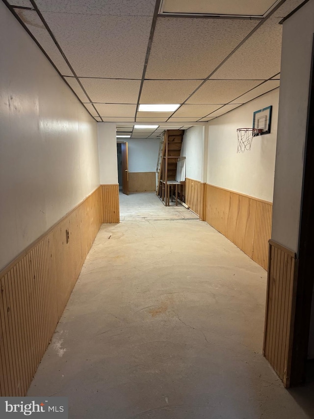 basement featuring a paneled ceiling and wood walls